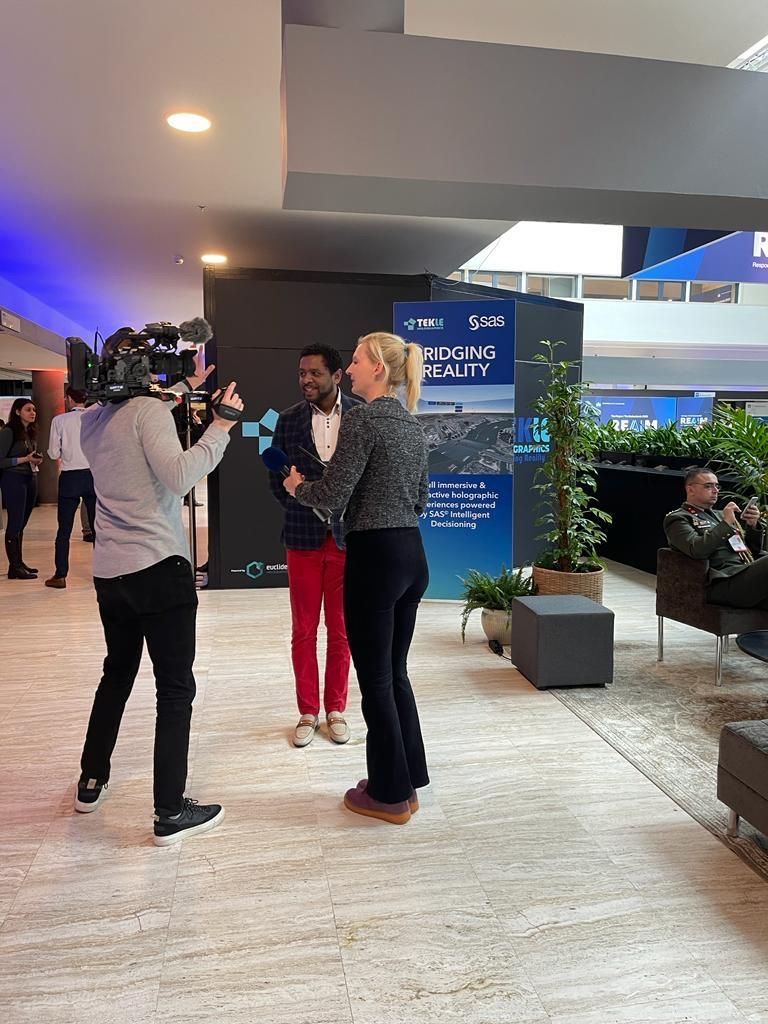 Michel Tzsfaldet being interviewed on camera at the REAIM 2023 summit, in front of a Tekle Holographics and SAS banner.